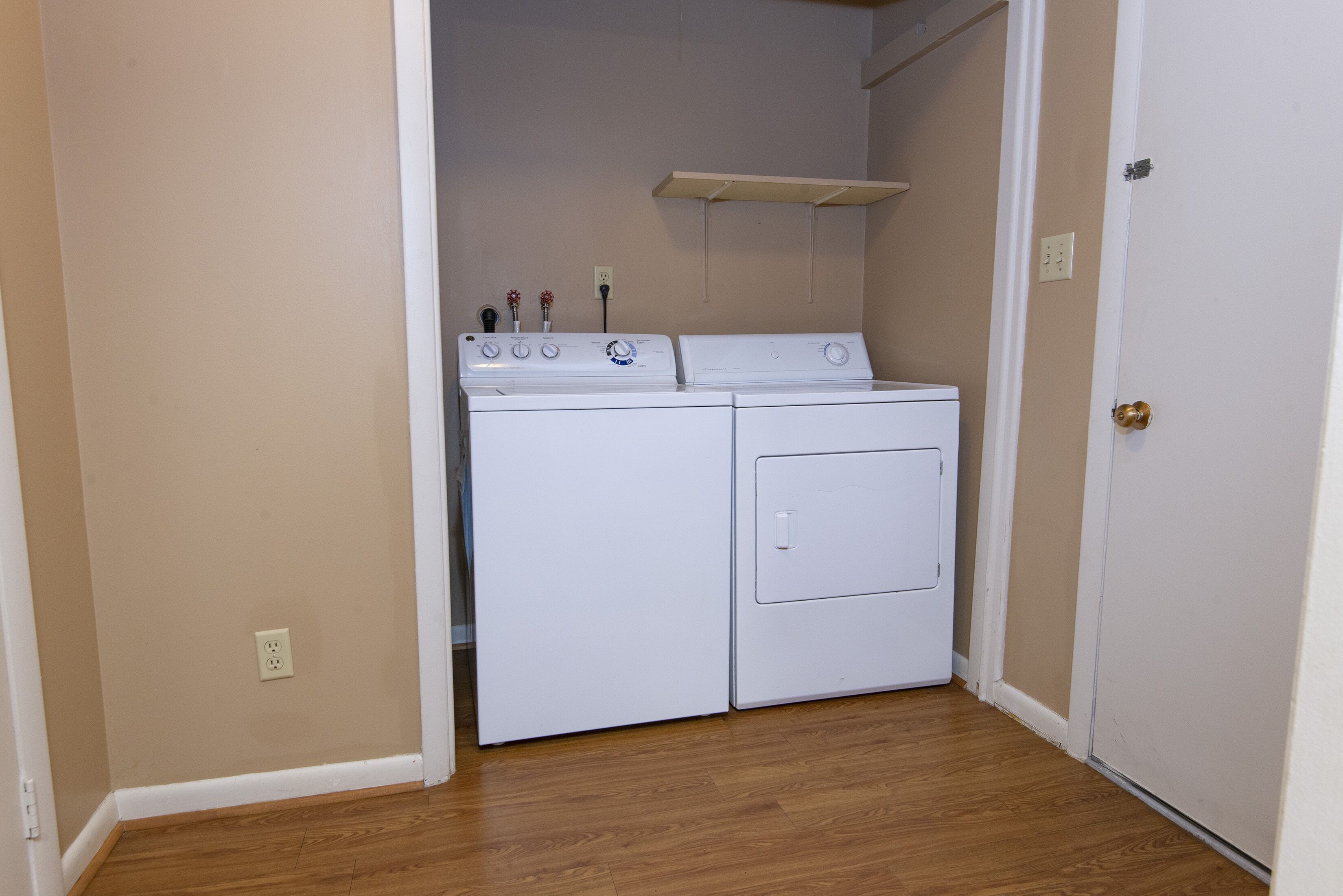 A laundry room with two white washers and dryers, wooden flooring, and a white door.
