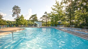 Une piscine à l’eau claire, entourée d’arbres et bordée d’une zone délimitée par une clôture, où se trouvent des chaises longues.