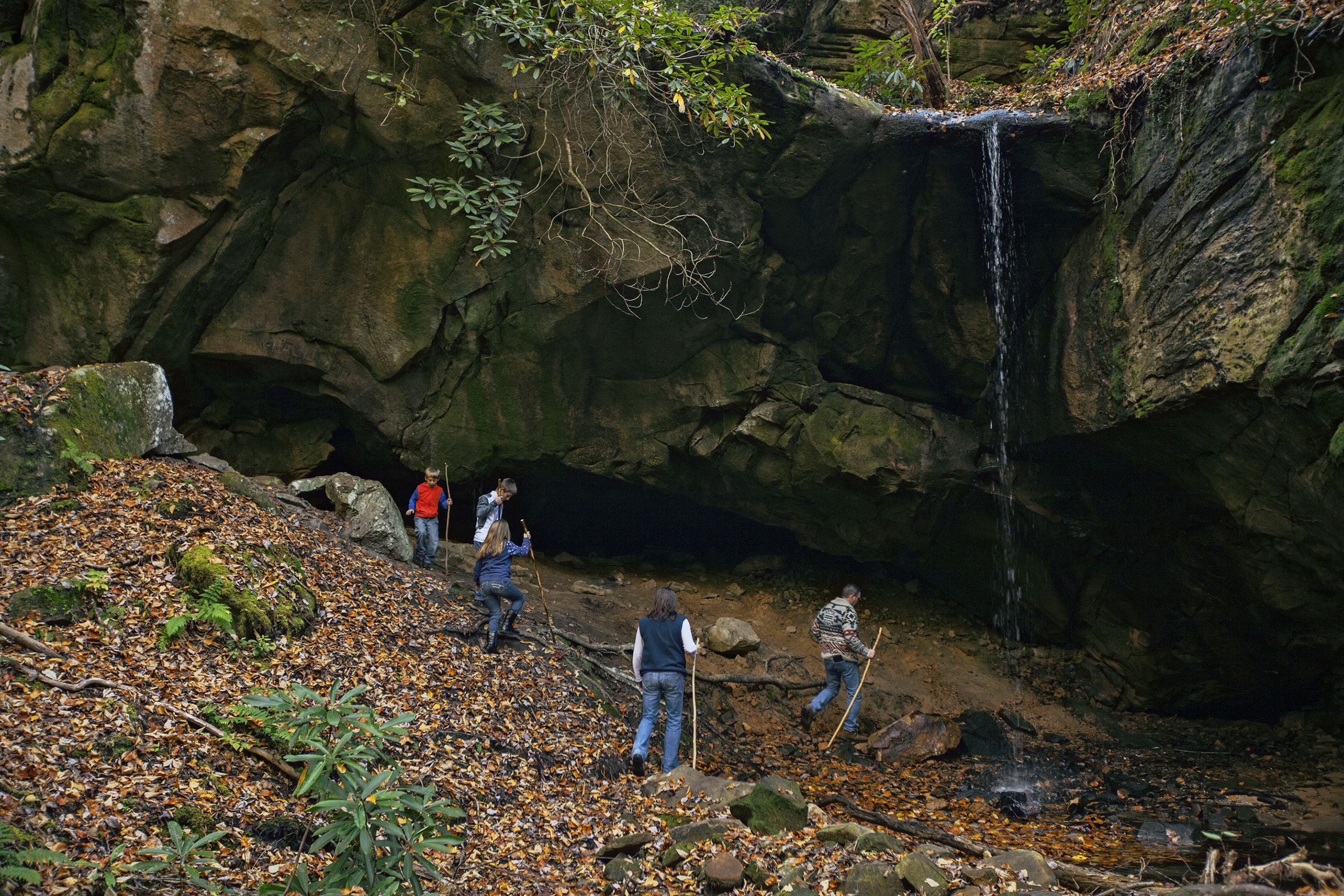 A group of people hiking near a waterfall in a rocky area with fallen leaves.