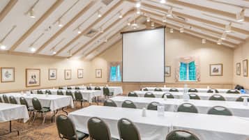 A conference room with multiple tables and chairs, a projector screen, and framed artwork on the walls.