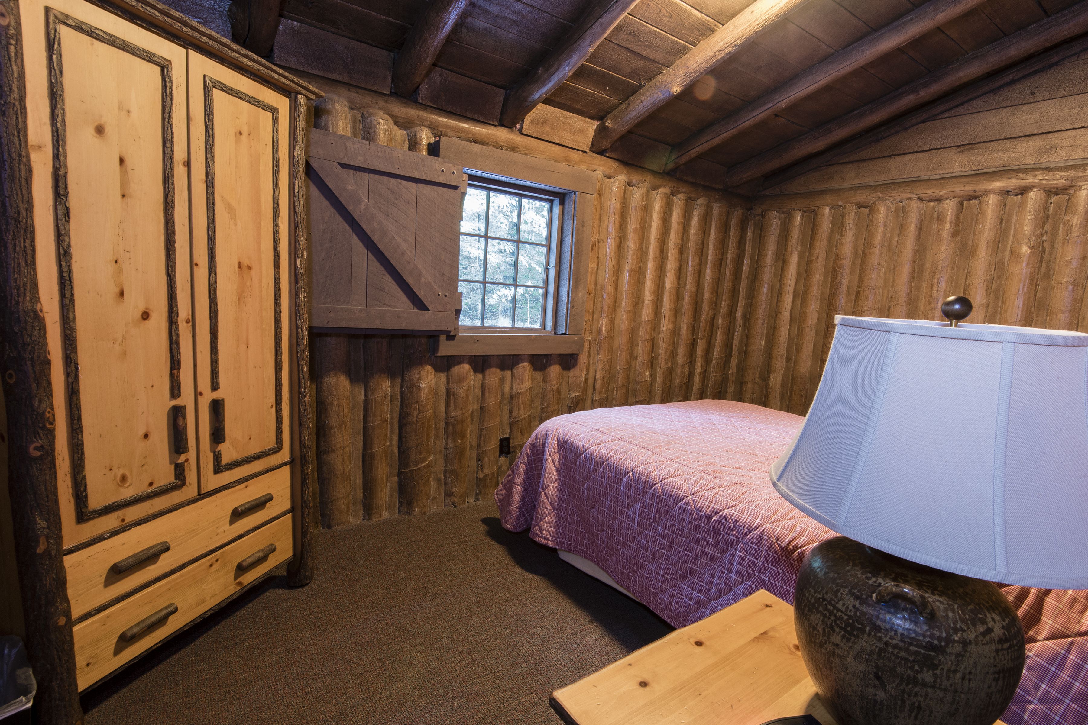 A wooden cabin room with a bed, a window, and a wooden cabinet.