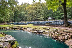 A natural setting with a clear pond surrounded by rocks and trees, and rows of blue chairs arranged for an event. - Pine Mountain State Resort Park (Pineville)
