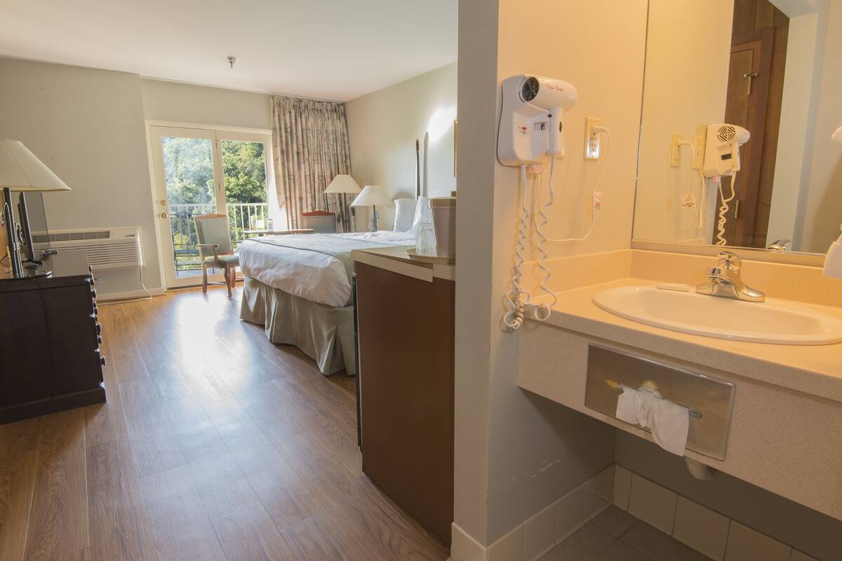 Ein Hotelzimmer mit Bett, Schreibtisch, Stuhl, Lampe, Haartrockner und einem Badezimmer mit Waschbecken und Spiegel.