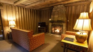 A cozy living room with a stone fireplace, two patterned armchairs, a small table with a lamp, and a television on a stand. - Pine Mountain State Resort Park (Pineville)