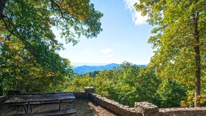 A picnic table and stone wall in a forested area with a view of distant mountains. - Pine Mountain State Resort Park (Pineville)