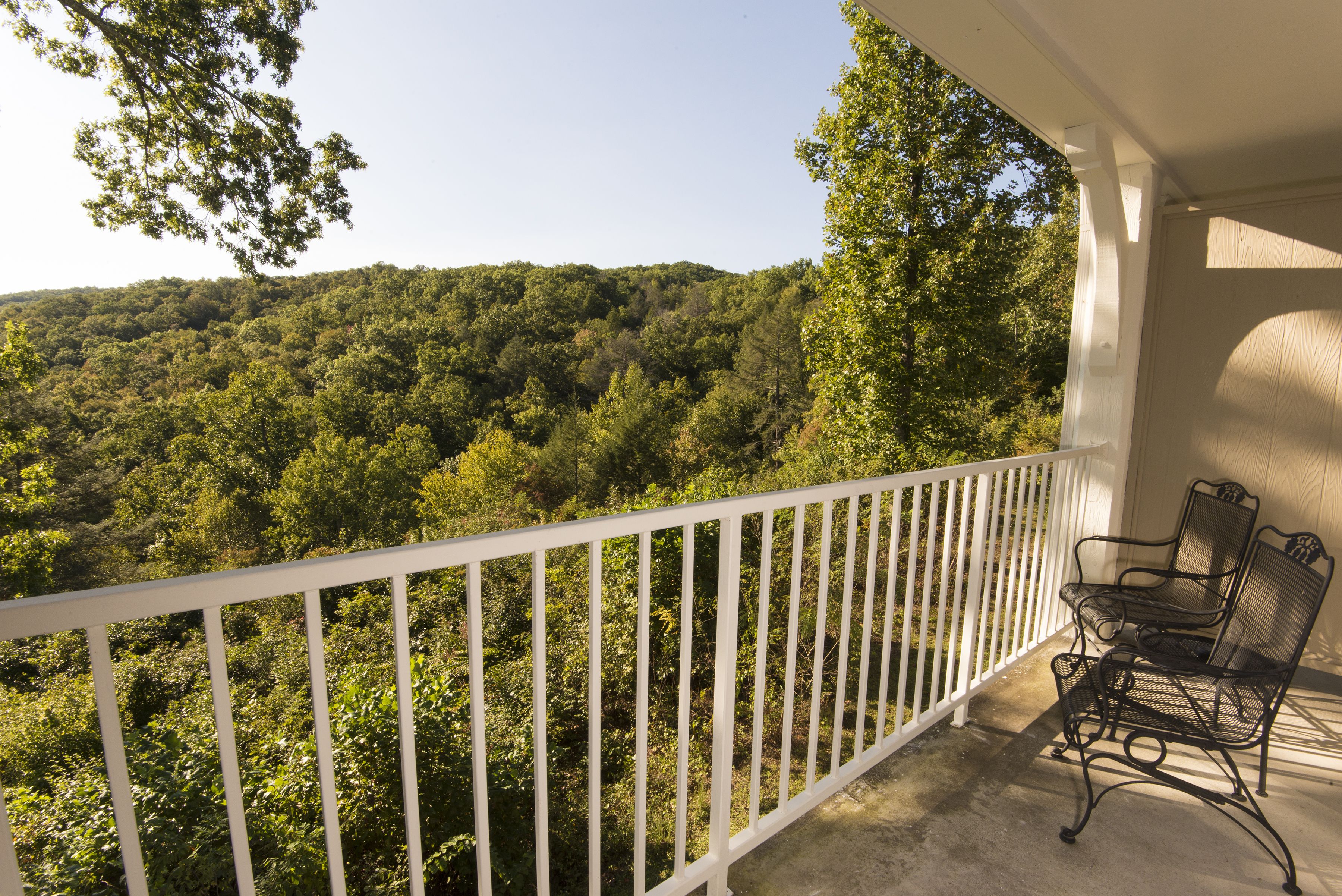 Un balcon doté d’une balustrade blanche, donnant sur une colline boisée.