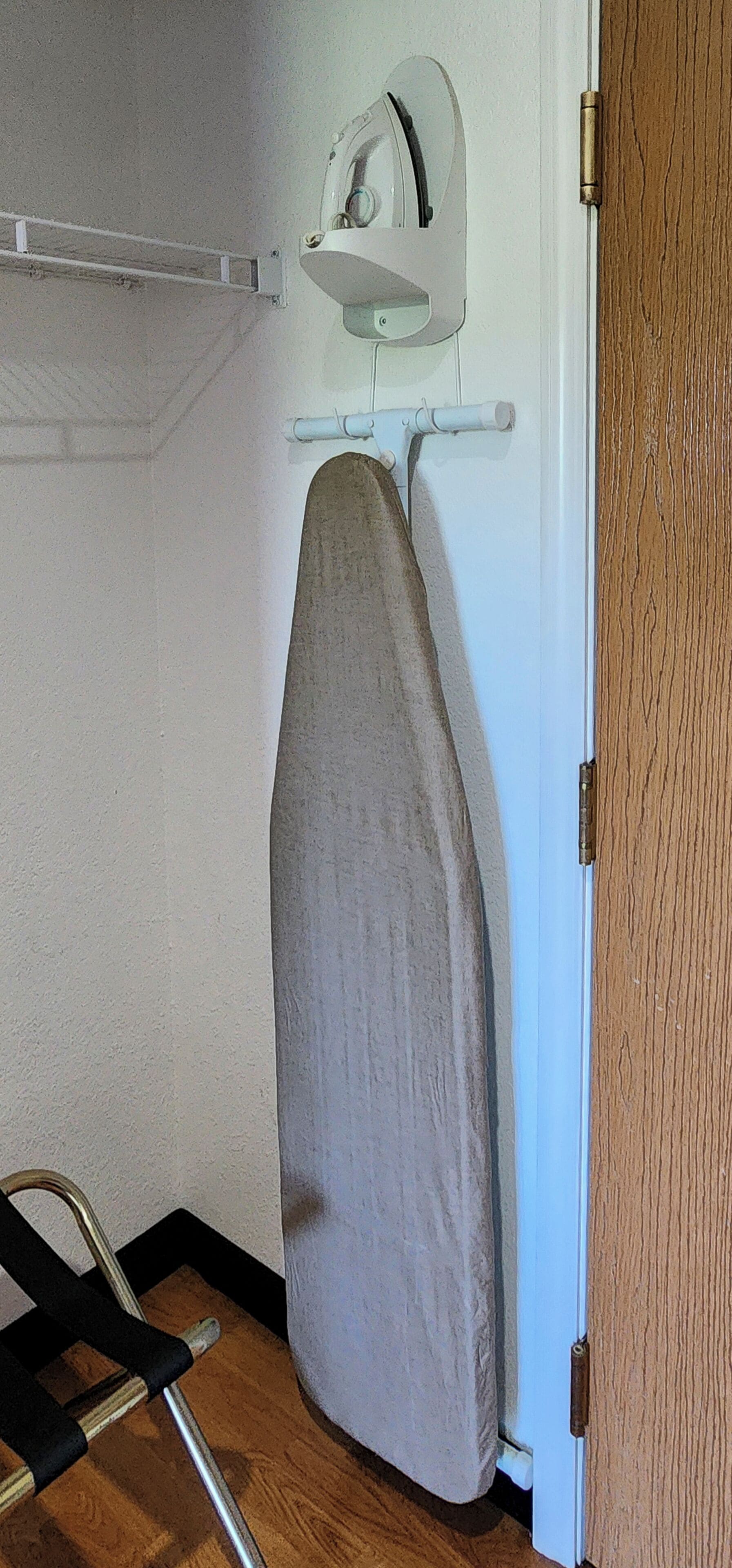 A room with a wooden floor, a white door, and a wall-mounted ironing board with an iron.