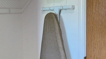 A room with a wooden floor, a white door, and a wall-mounted ironing board with an iron.