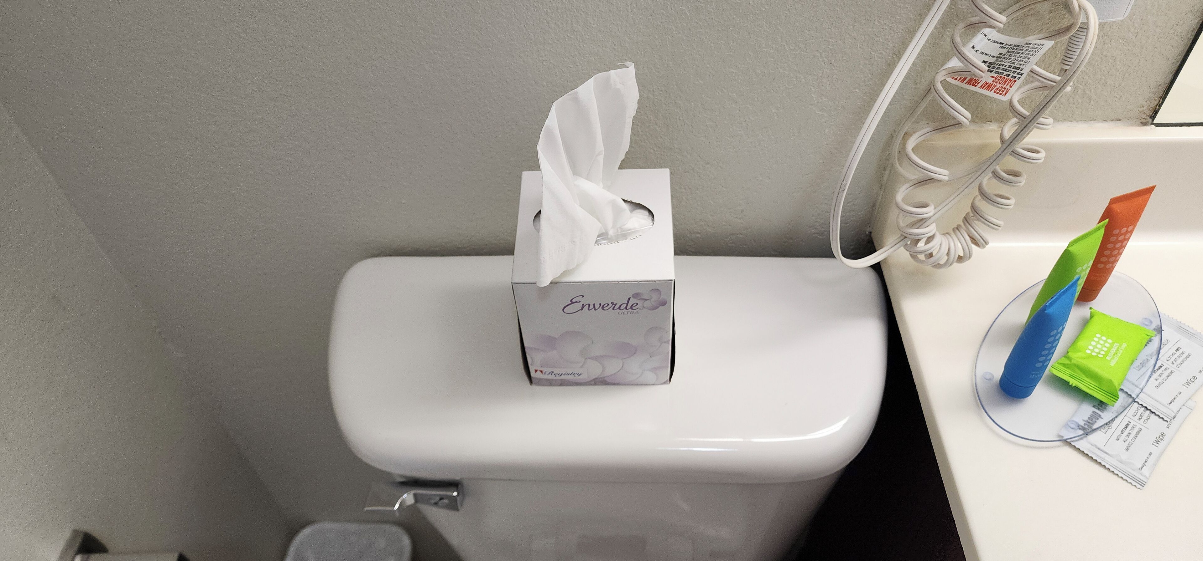 Toilette mit einer Tissuebox mit dem Aufdruck 'Enviro' und einem Tissue-Spender mit blauem und grünem Handdesinfektionsmittel.