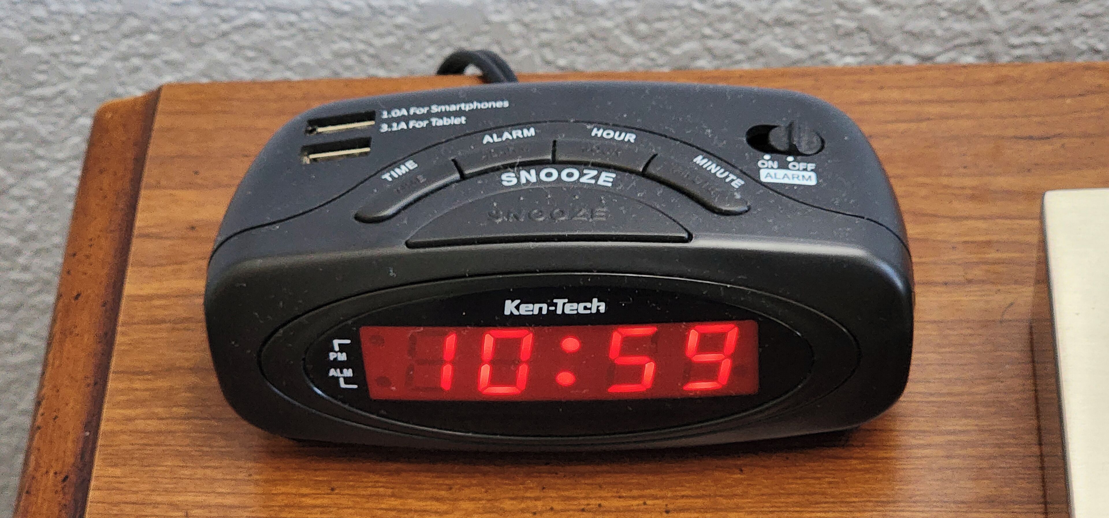 A Ken-Tech alarm clock with a digital display on a wooden surface.