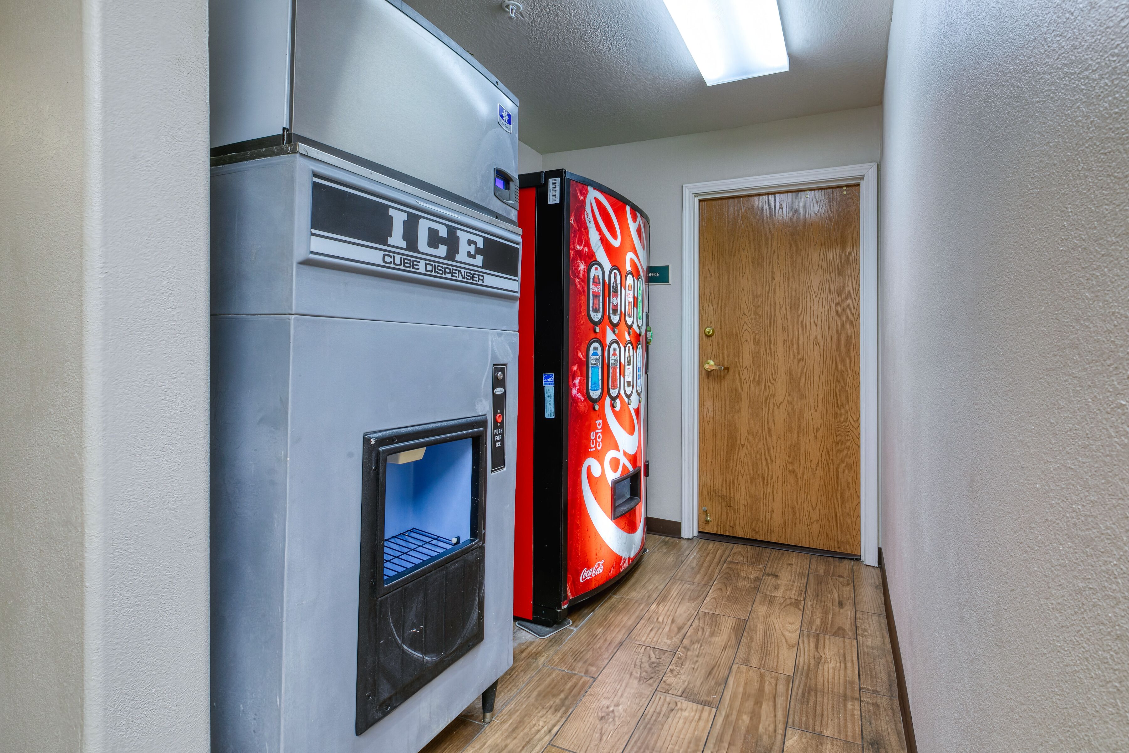 A hallway with a vending machine labeled "ICE CUBE DISPENSER" and a Coca-Cola refrigerator.