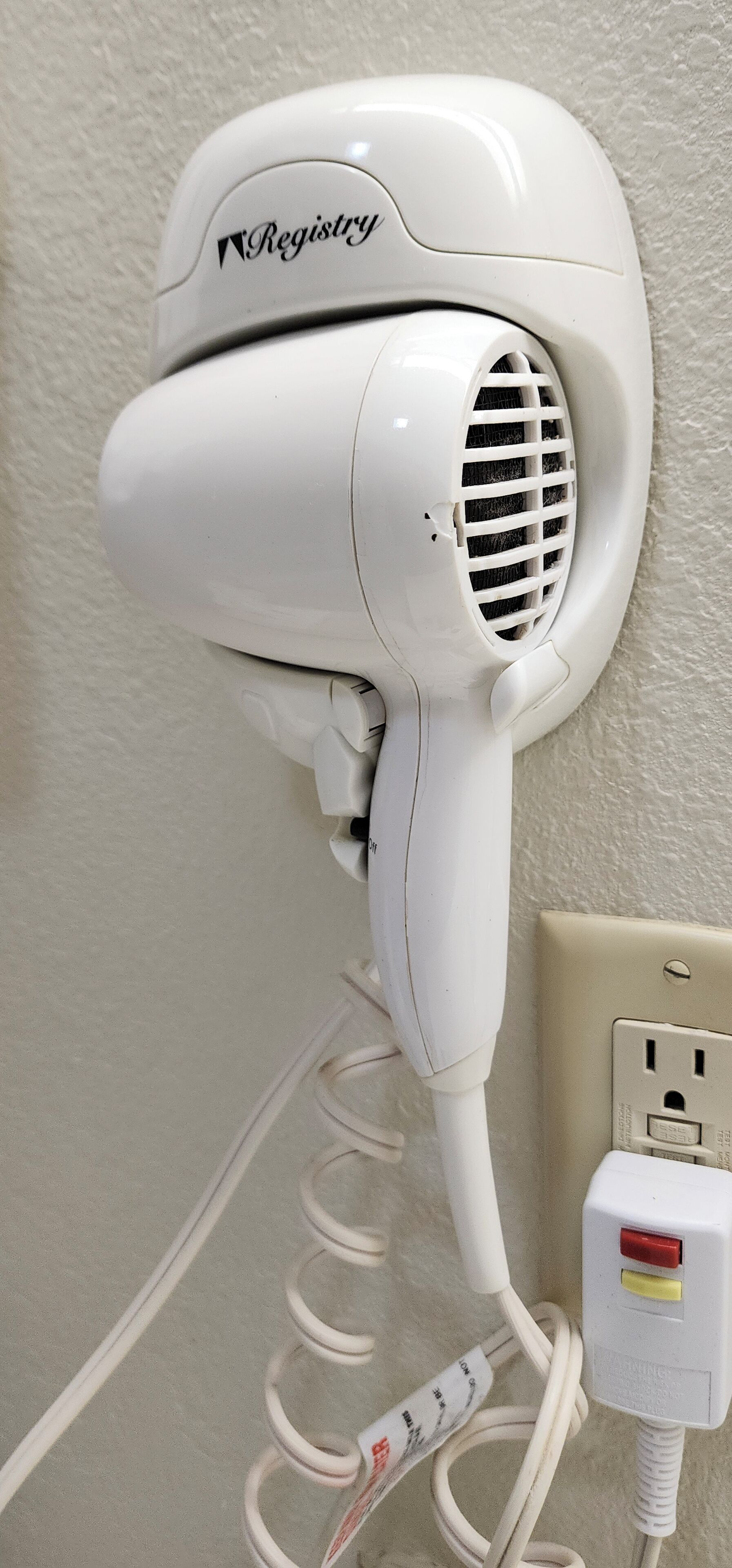 Un sèche-cheveux blanc fixé au mur, branché à une prise de courant.