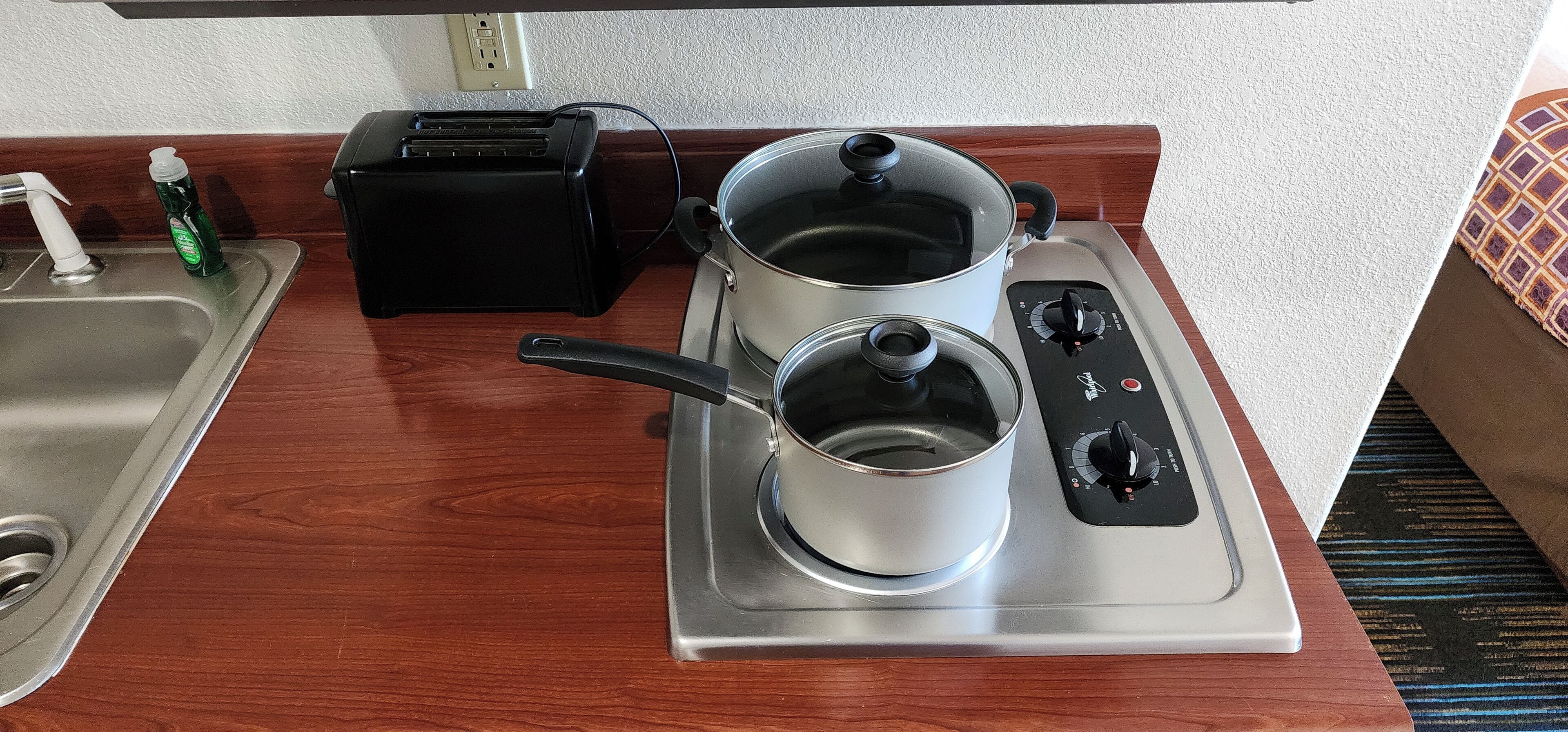 A kitchenette with a stainless steel sink, a toaster, a stovetop with pots, and a power outlet.