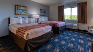 Habitación de hotel con dos camas, un ventanal con cortinas, un radiador y dos cuadros en la pared.