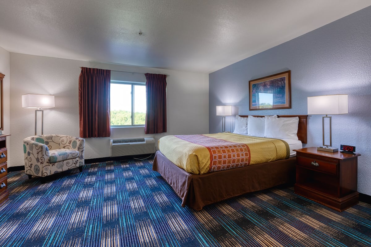 A hotel room with a bed, two bedside tables, a chair, a window with curtains, and a painting on the wall.