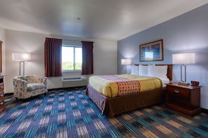 A hotel room with a bed, two bedside tables, a chair, a window with curtains, and a painting on the wall.