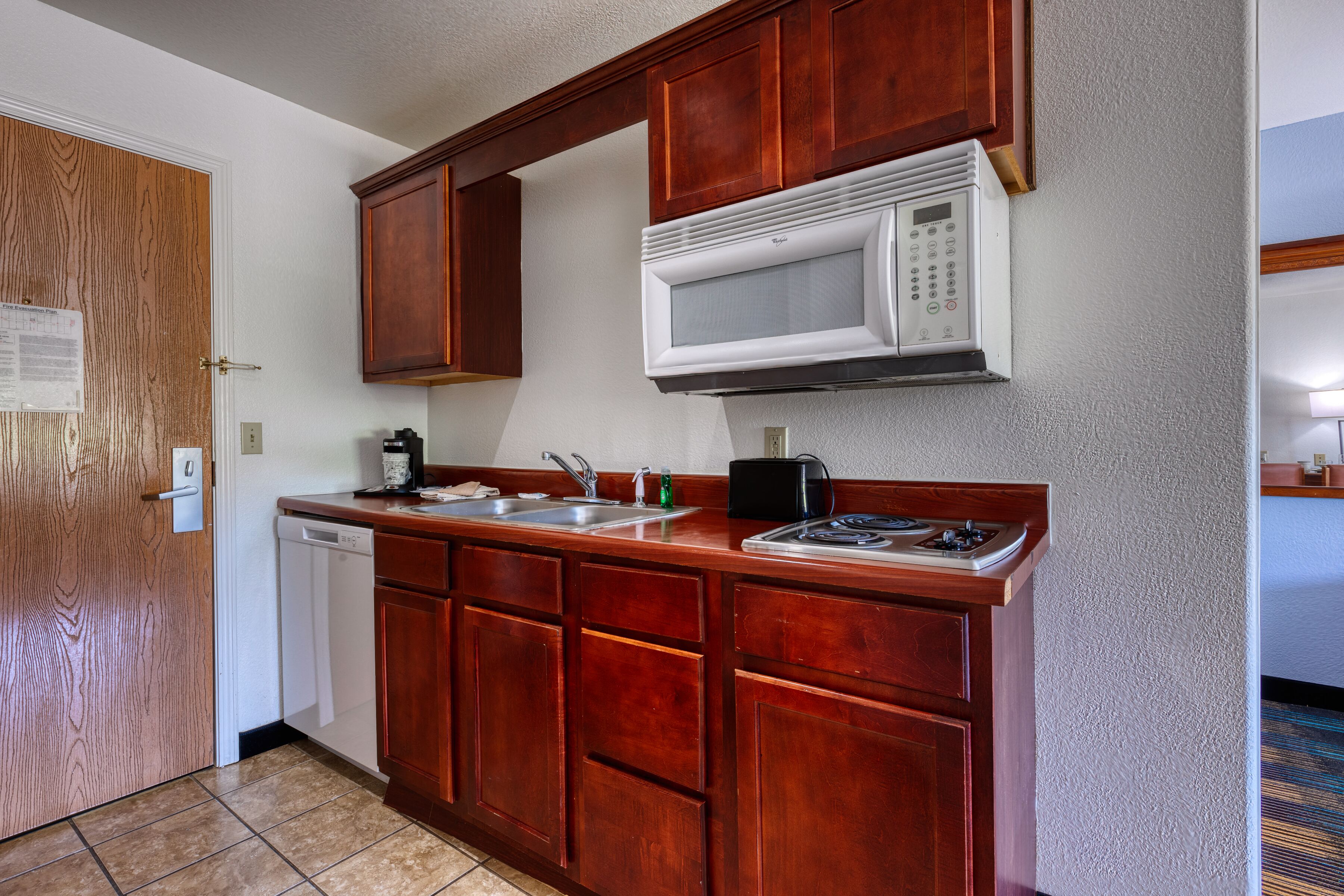 Una cocina compacta con armarios de madera, un microondas integrado, lavavajillas y una placa de cocina.