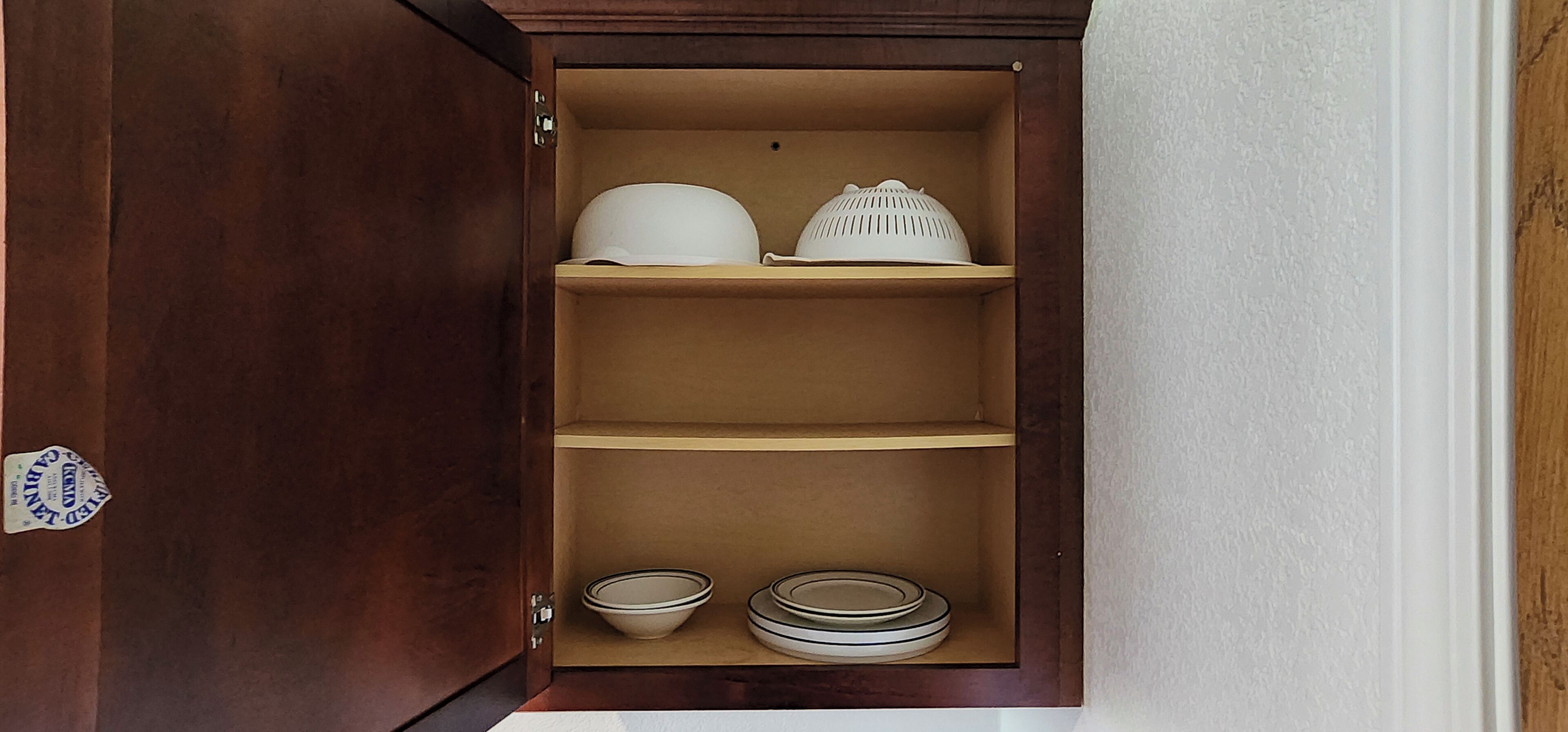 A wooden cabinet with three shelves, each containing kitchenware.