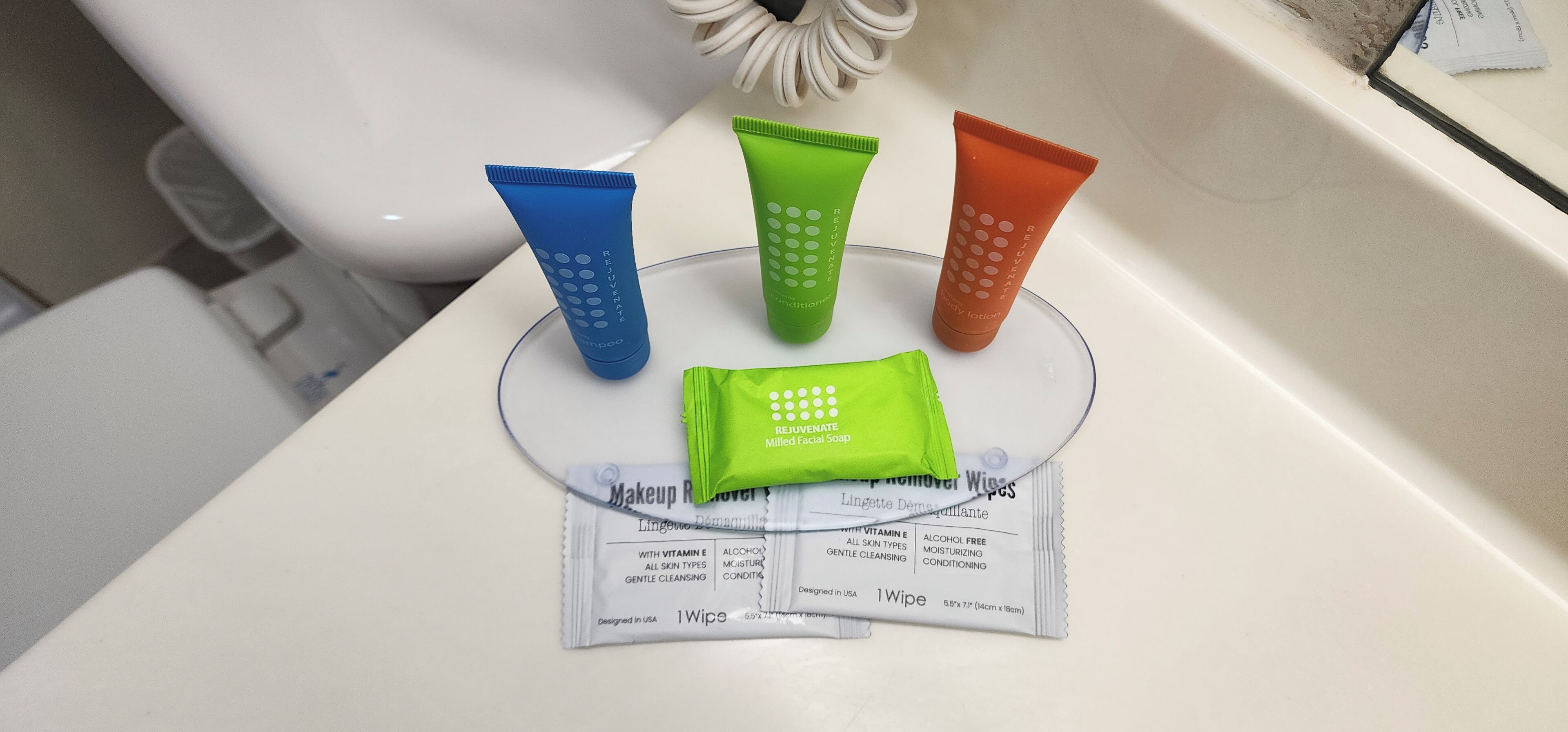 A bathroom sink with four colorful tubes of makeup remover wipes and a packet of facial soap.