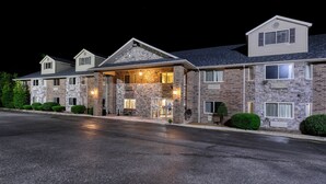 Un hotel de varios pisos con fachada de piedra, entrada cubierta y estacionamiento.