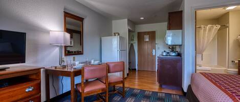 Une chambre d’hôtel de taille réduite, comprenant un lit, un bureau avec une chaise, une télévision, un réfrigérateur, un four à micro-ondes et une salle de bain avec un rideau de douche.