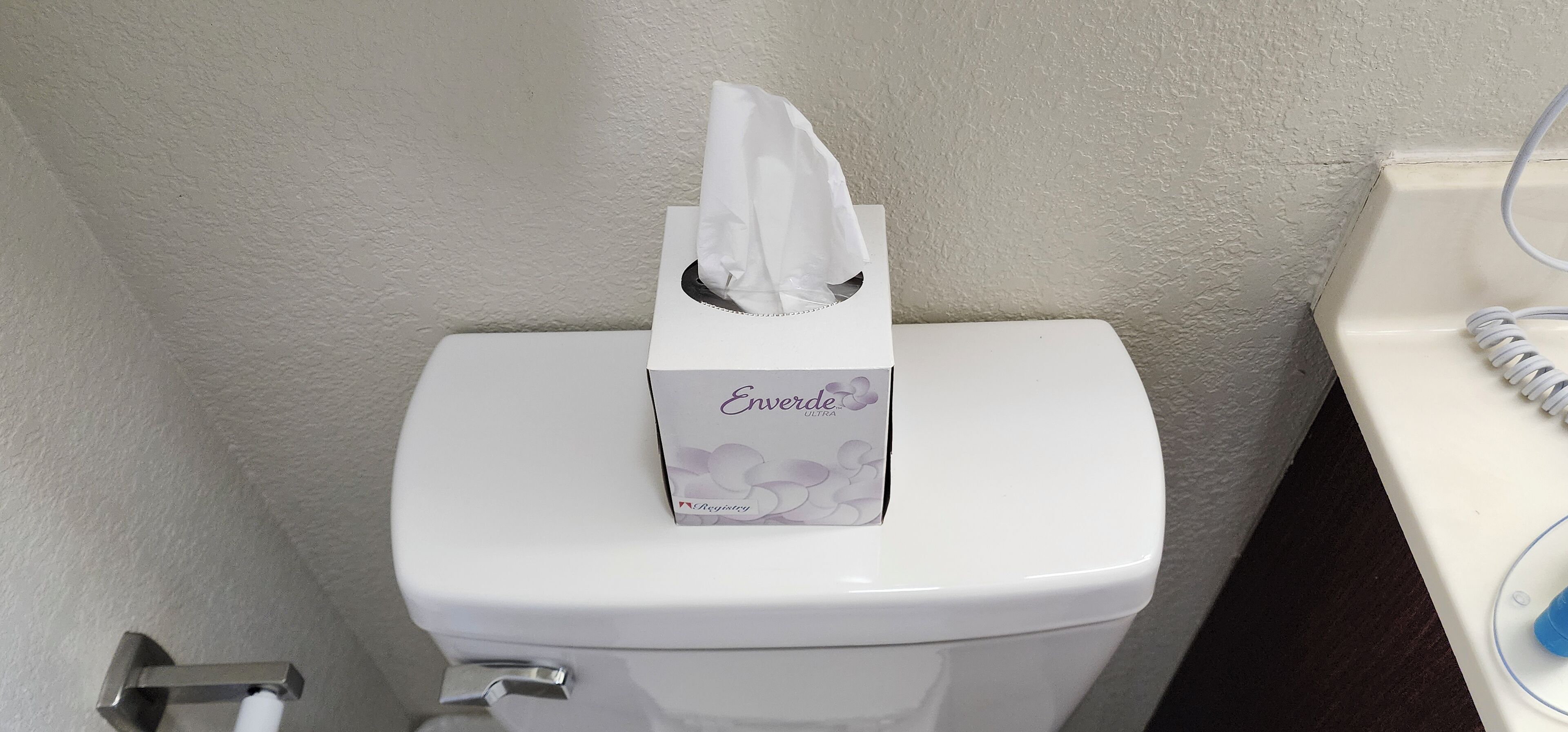 Un inodoro con una caja de pañuelos etiquetada como "Enverde Ultra" encima.