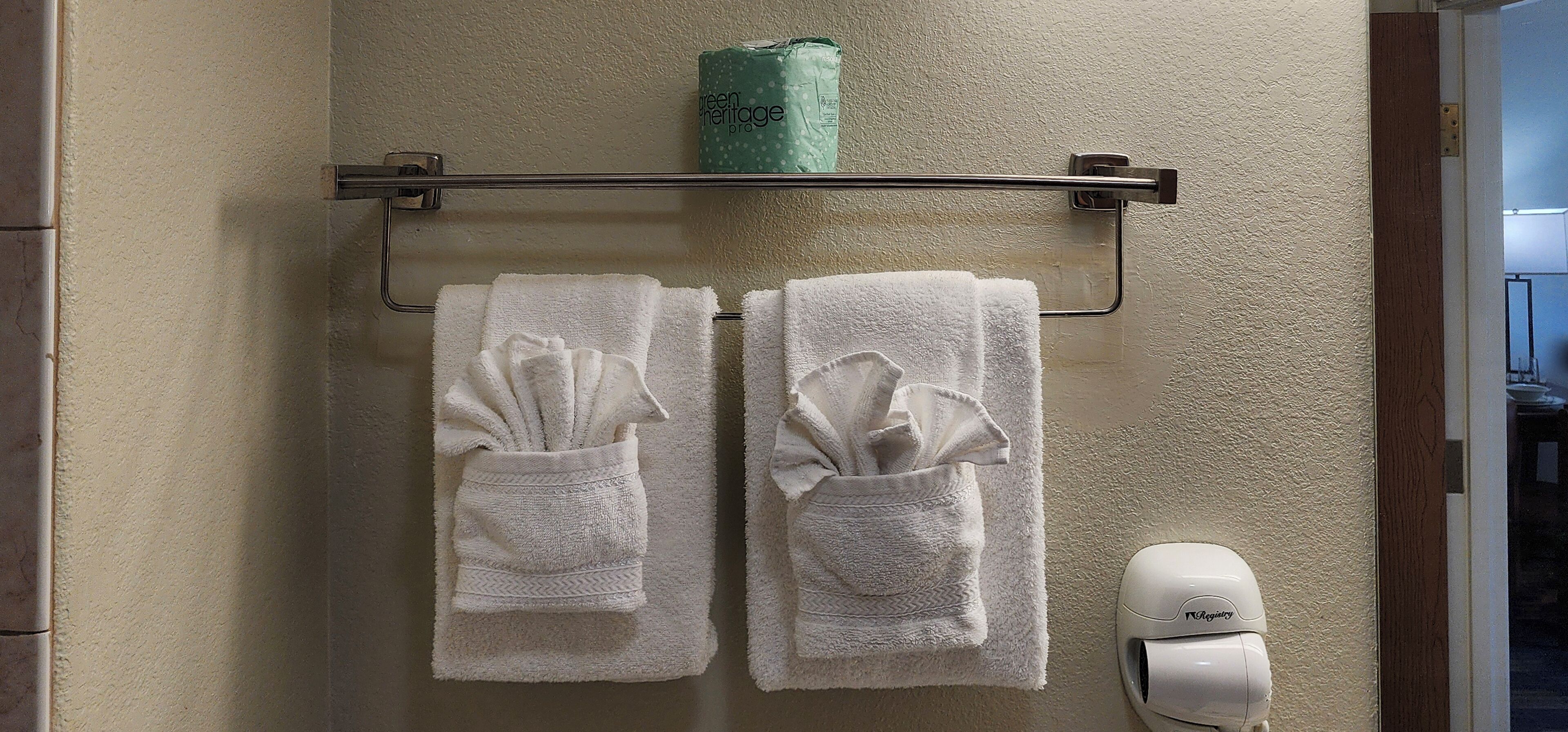 A bathroom with two white towels hanging on a metal towel rack, a green package on the wall, and a white hand dryer.