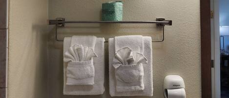 A bathroom with two white towels hanging on a metal towel rack, a green package on the wall, and a white hand dryer.