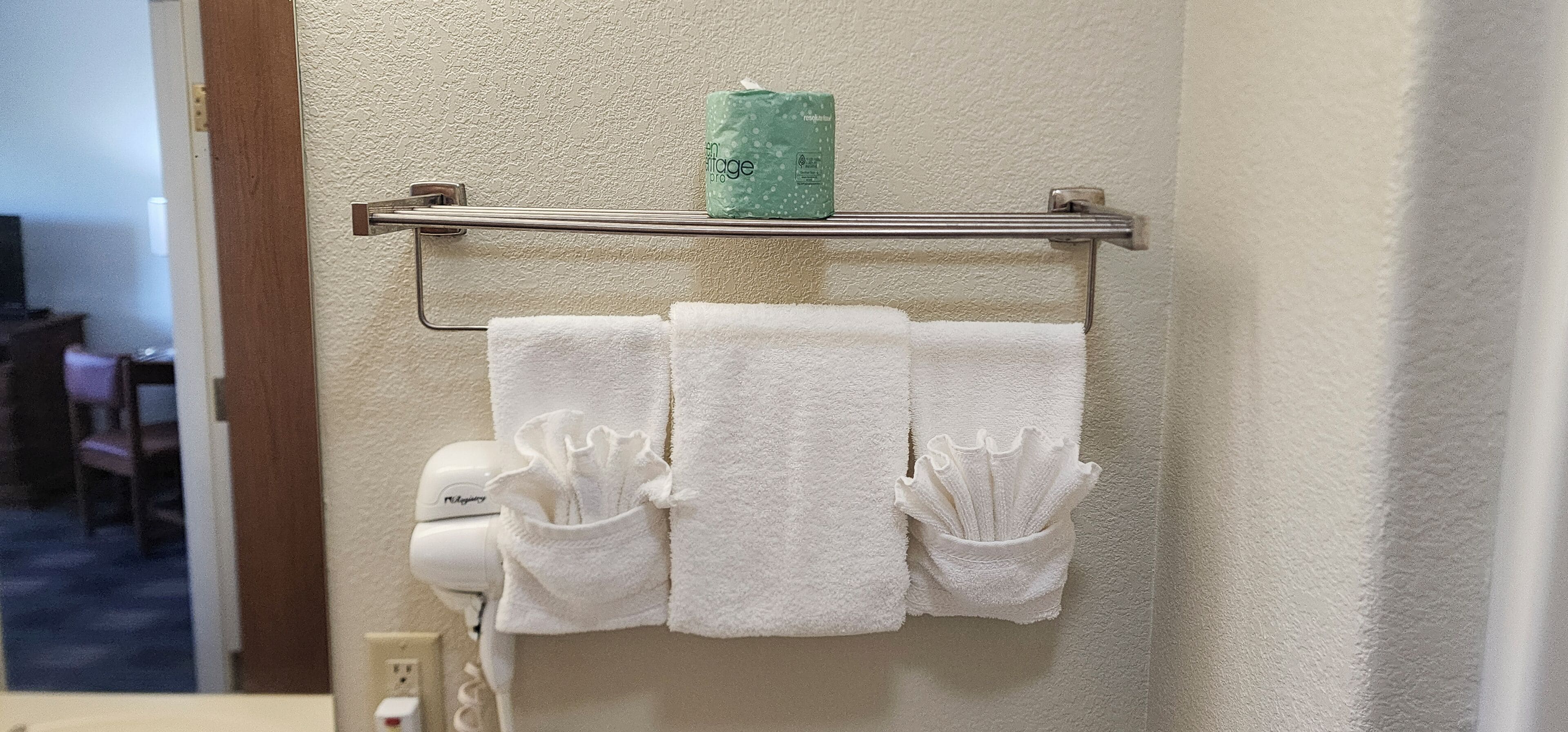 A bathroom with a towel rack holding three white towels and a green bottle of lotion.