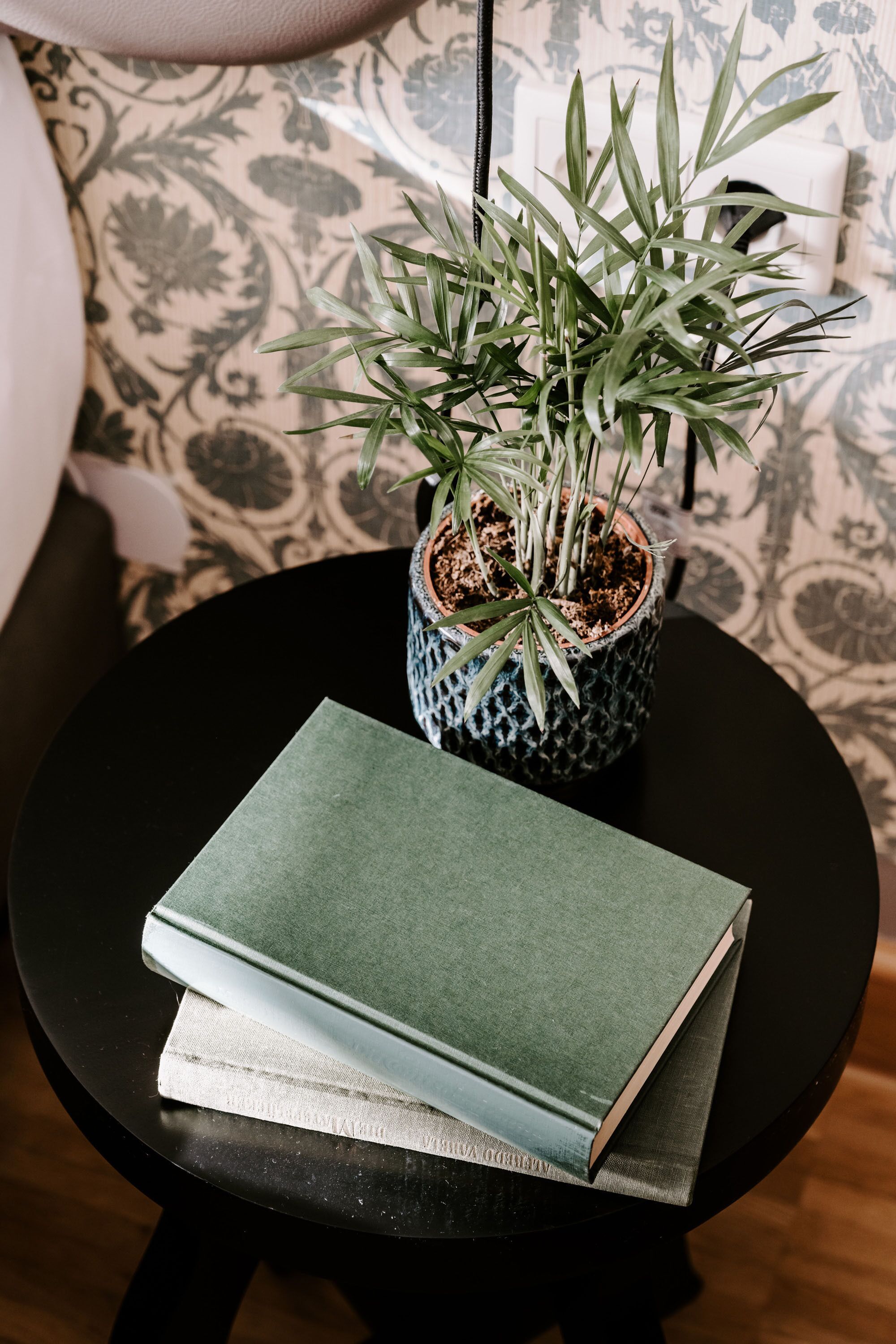 Ein kleiner runder Tisch mit einem Blumentopf und zwei Büchern darauf.