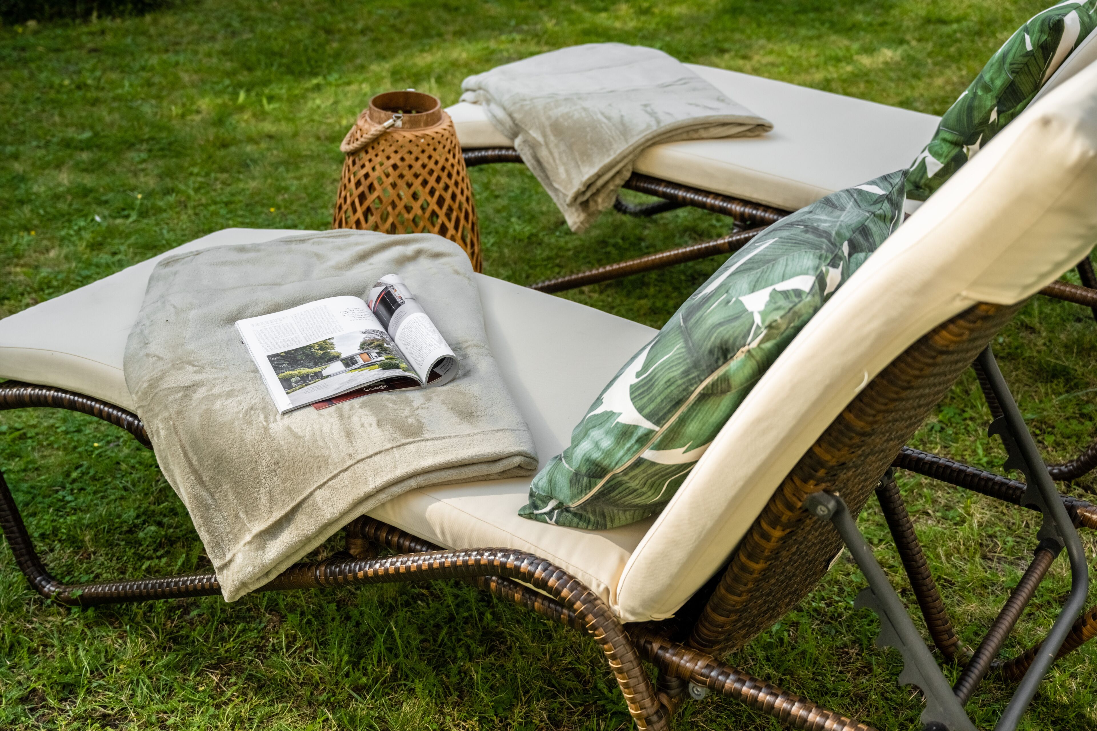 Una silla de mimbre con cojín y una revista, sobre un césped.