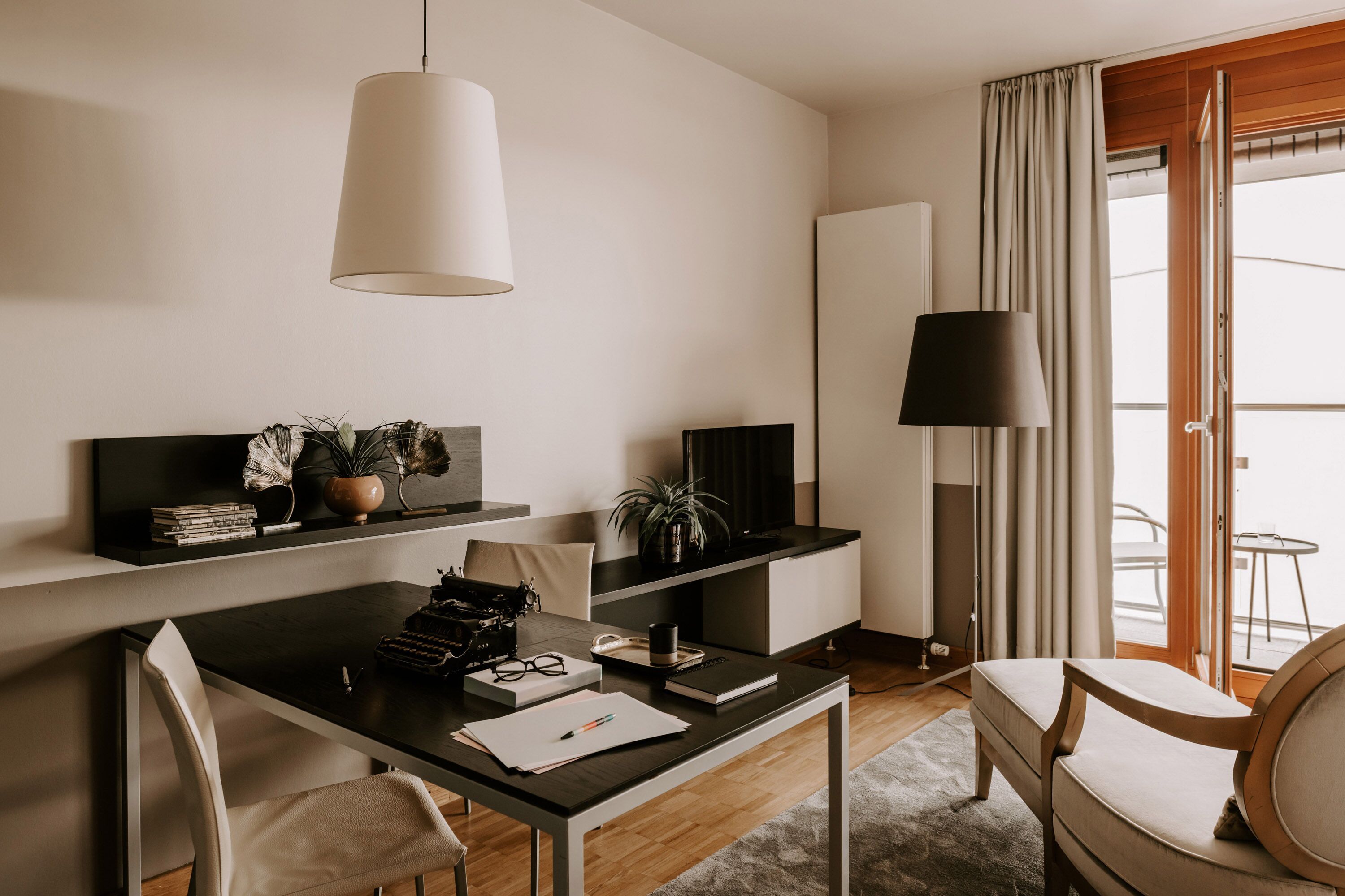 Una habitación de hotel moderna con escritorio, silla y un ventanal con cortinas.