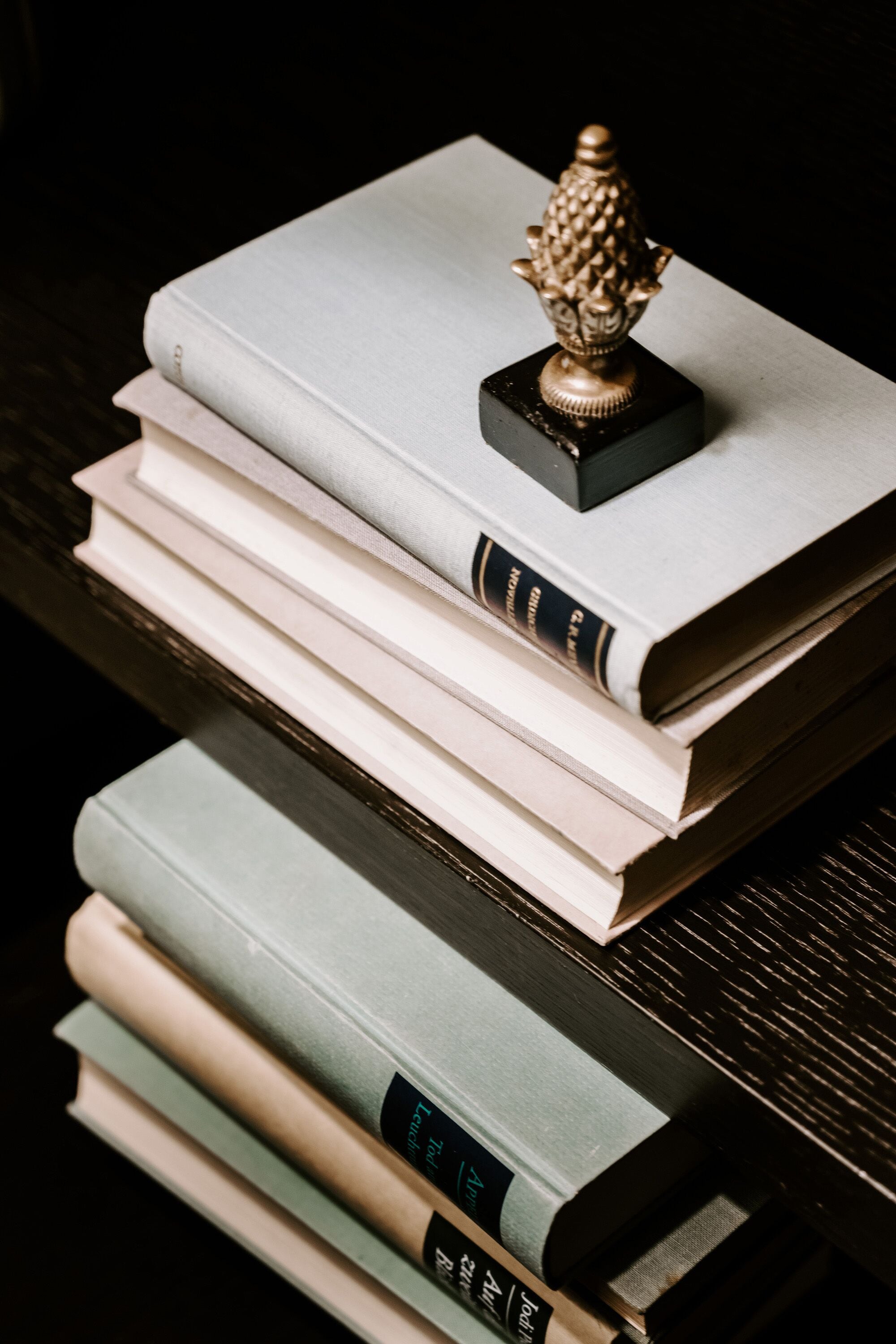 Una pila de libros con un objeto decorativo encima, sobre una superficie oscura.