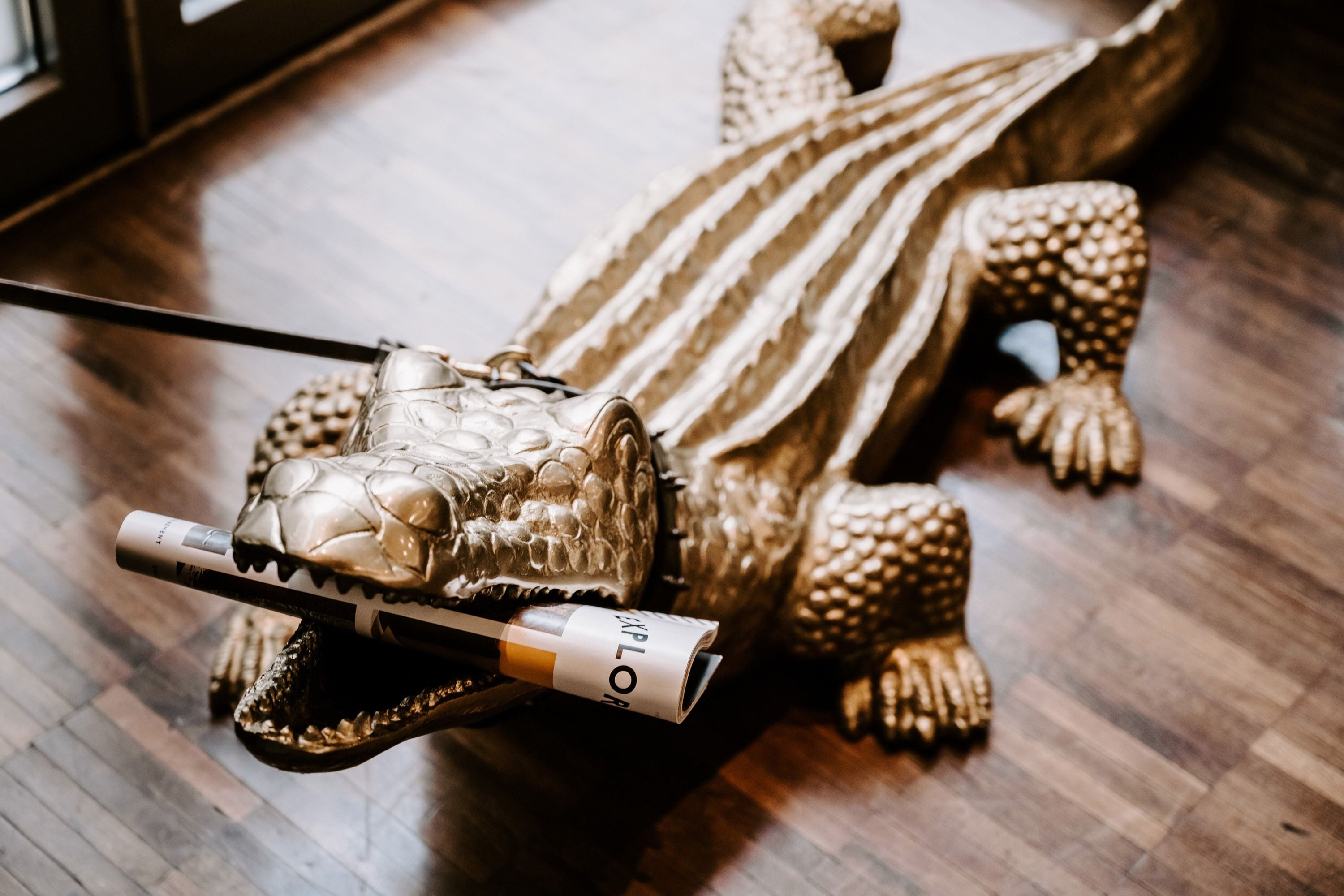 A golden crocodile sculpture with a magazine on its tail.