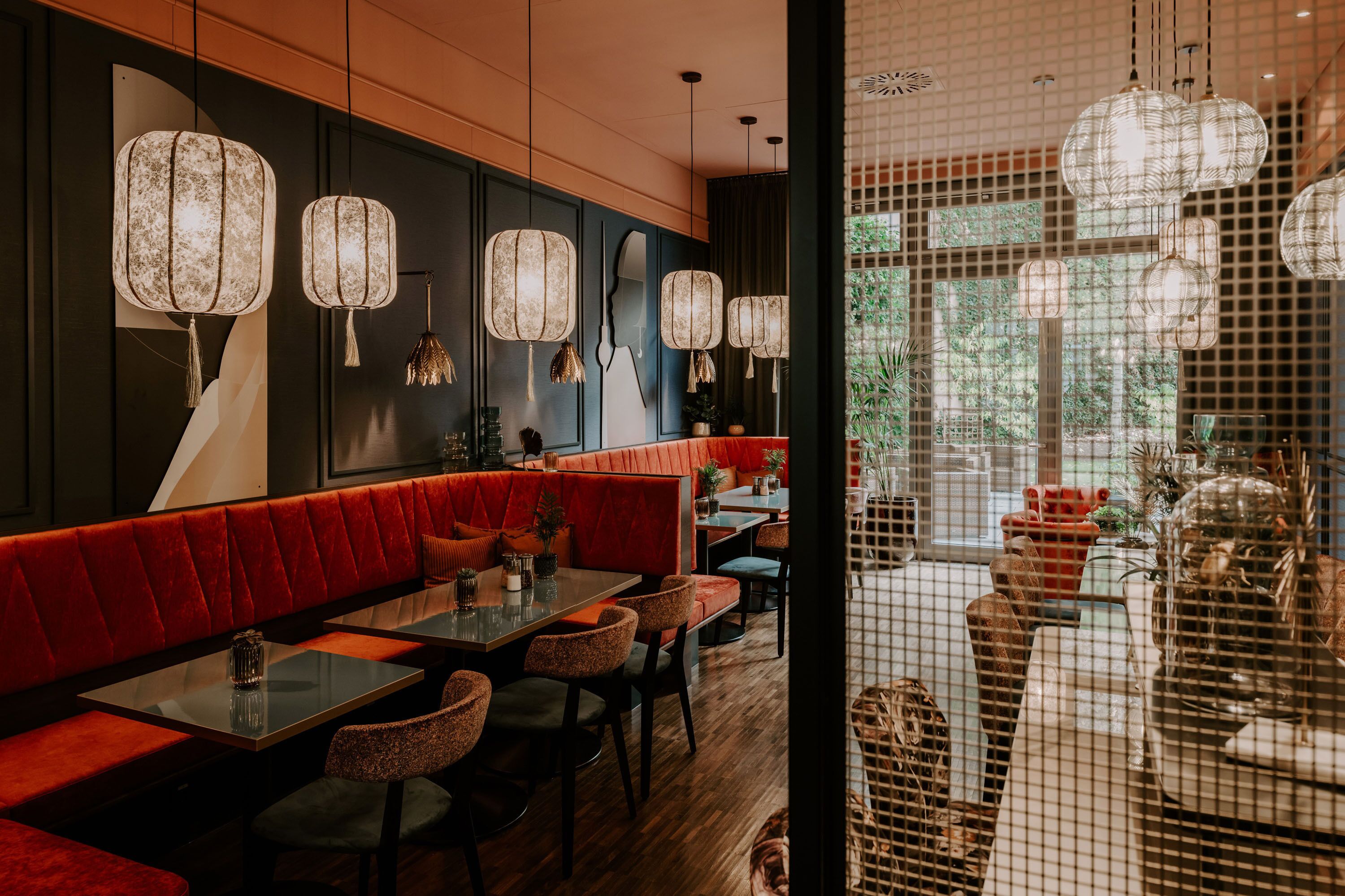 Un restaurante con asientos acolchados de color rojo, mesas con sillas y farolillos de papel colgantes.