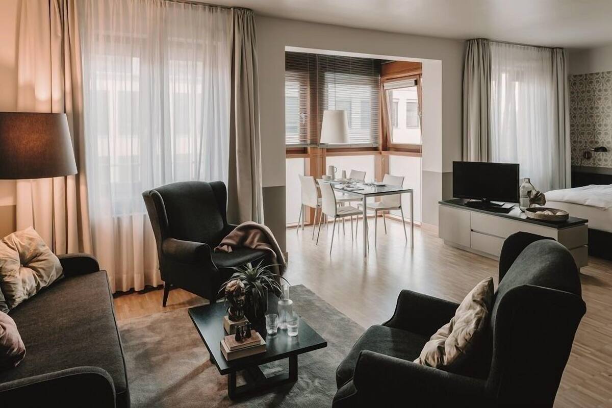 A modern hotel room with a living area, dining space, and a bed.