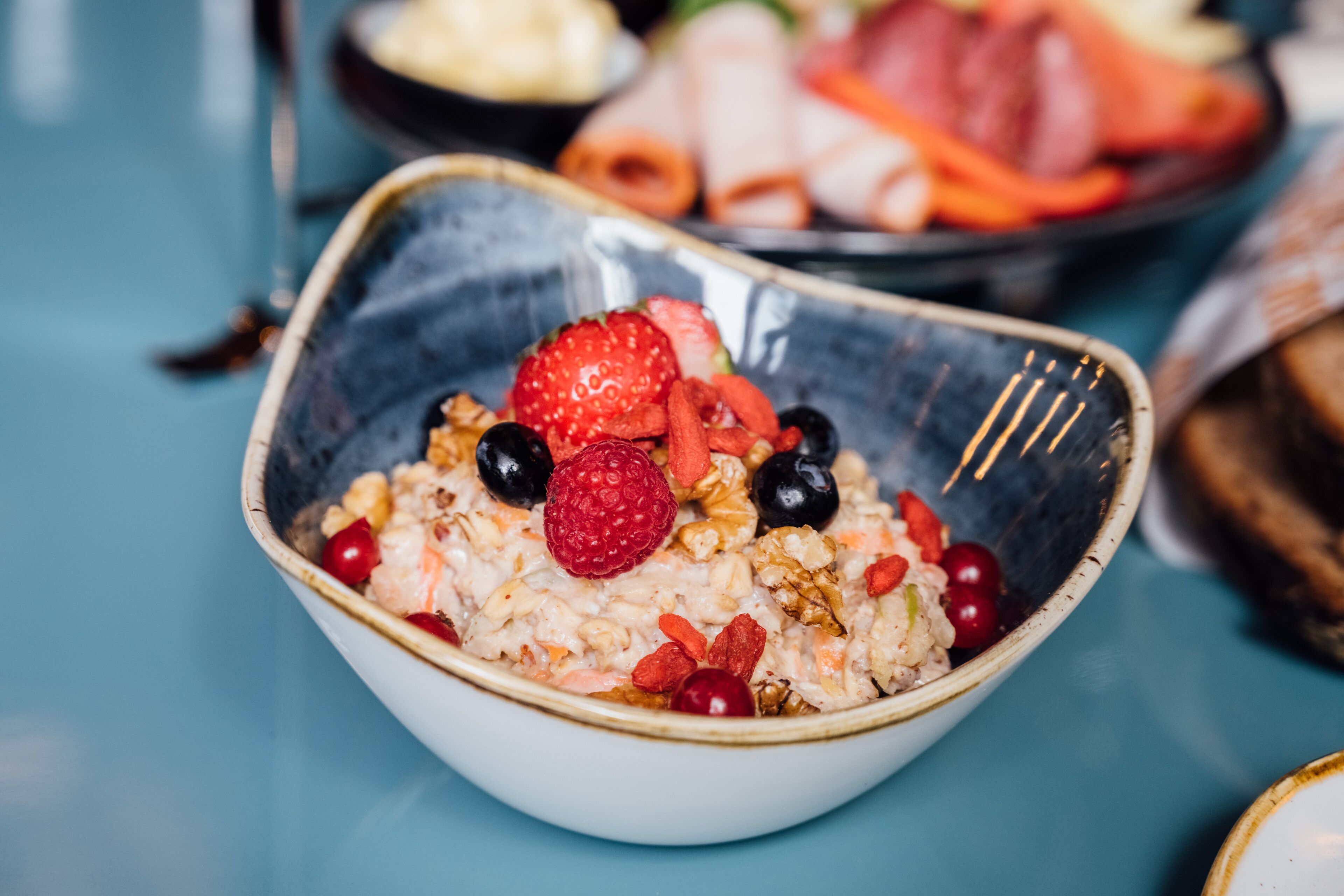 Un bol de porridge aux fruits rouges et aux noix, posé sur une table bleue.
