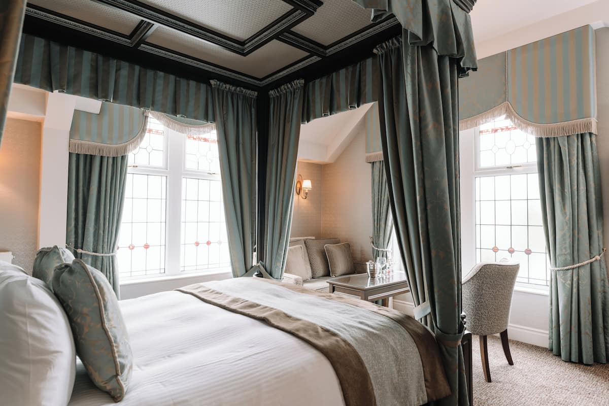 A bedroom with a large bed, a chair, a small table, and curtains.