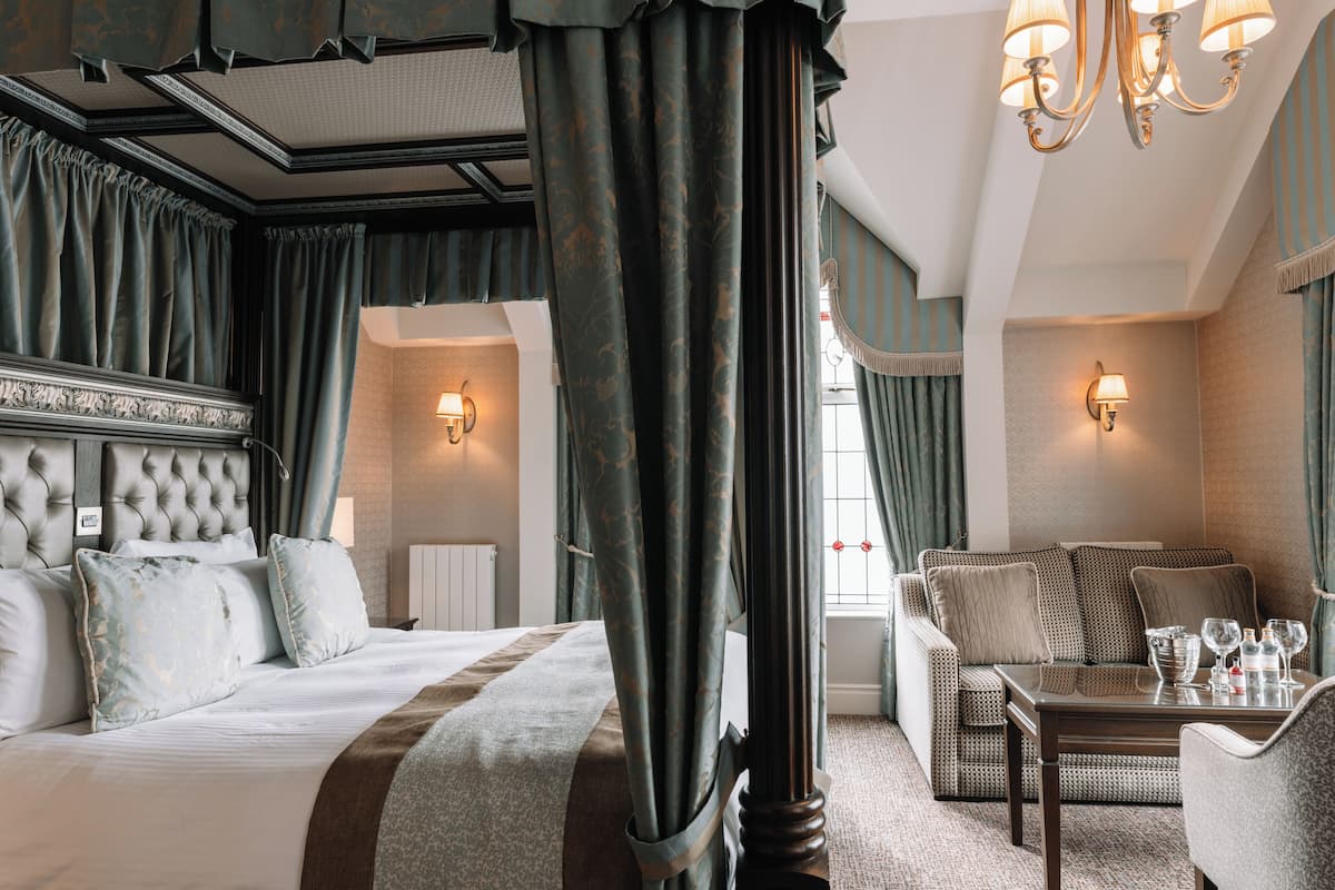 A hotel room with a large bed, a sitting area with a sofa and a table, and a window with curtains.