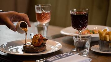 A dining table with plates of food, glasses of water and wine, and a hand pouring sauce.