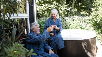 Two people in blue robes sitting by a hot tub outdoors, surrounded by greenery.