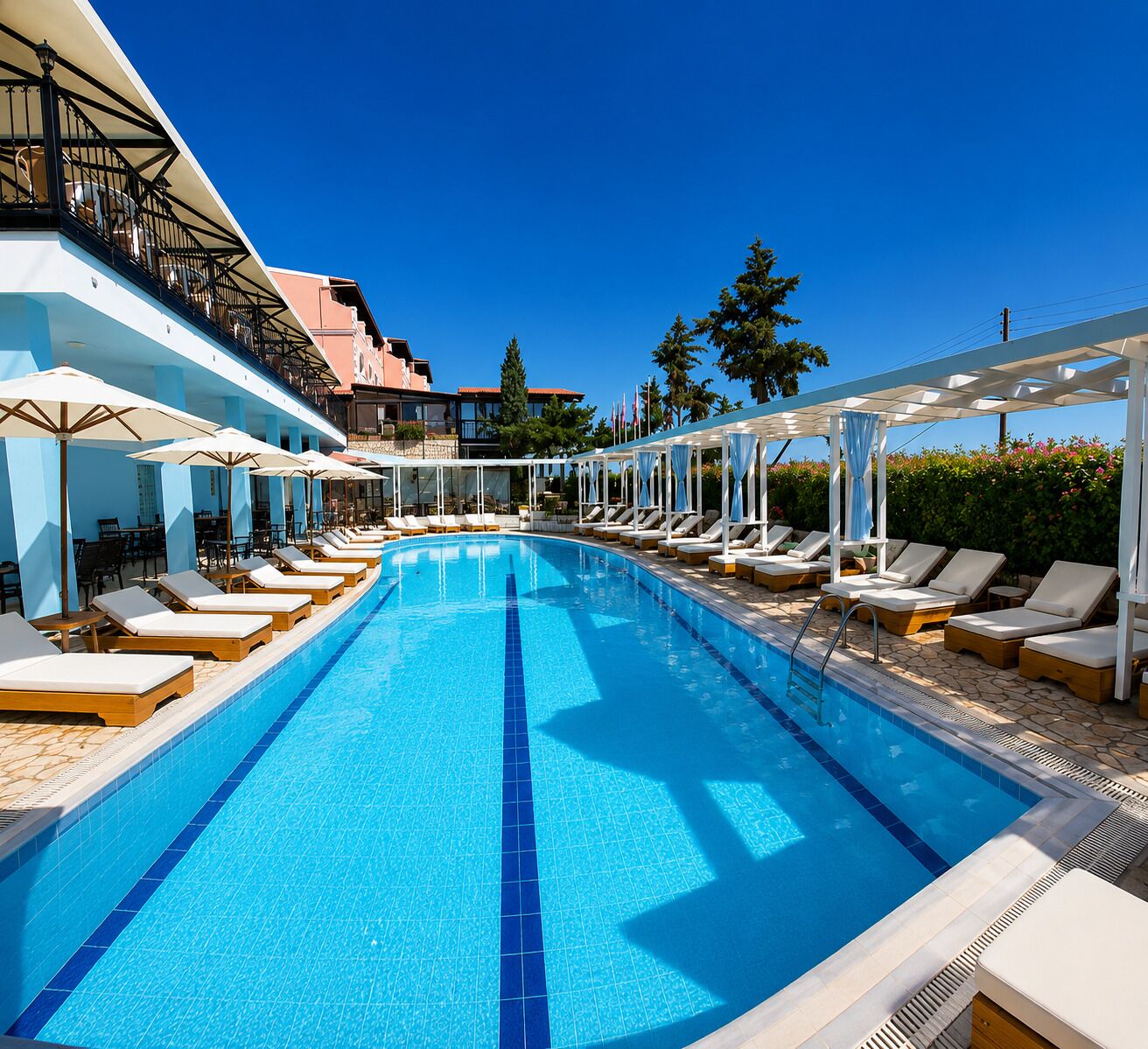 A swimming pool with lounge chairs and umbrellas, surrounded by buildings and trees.