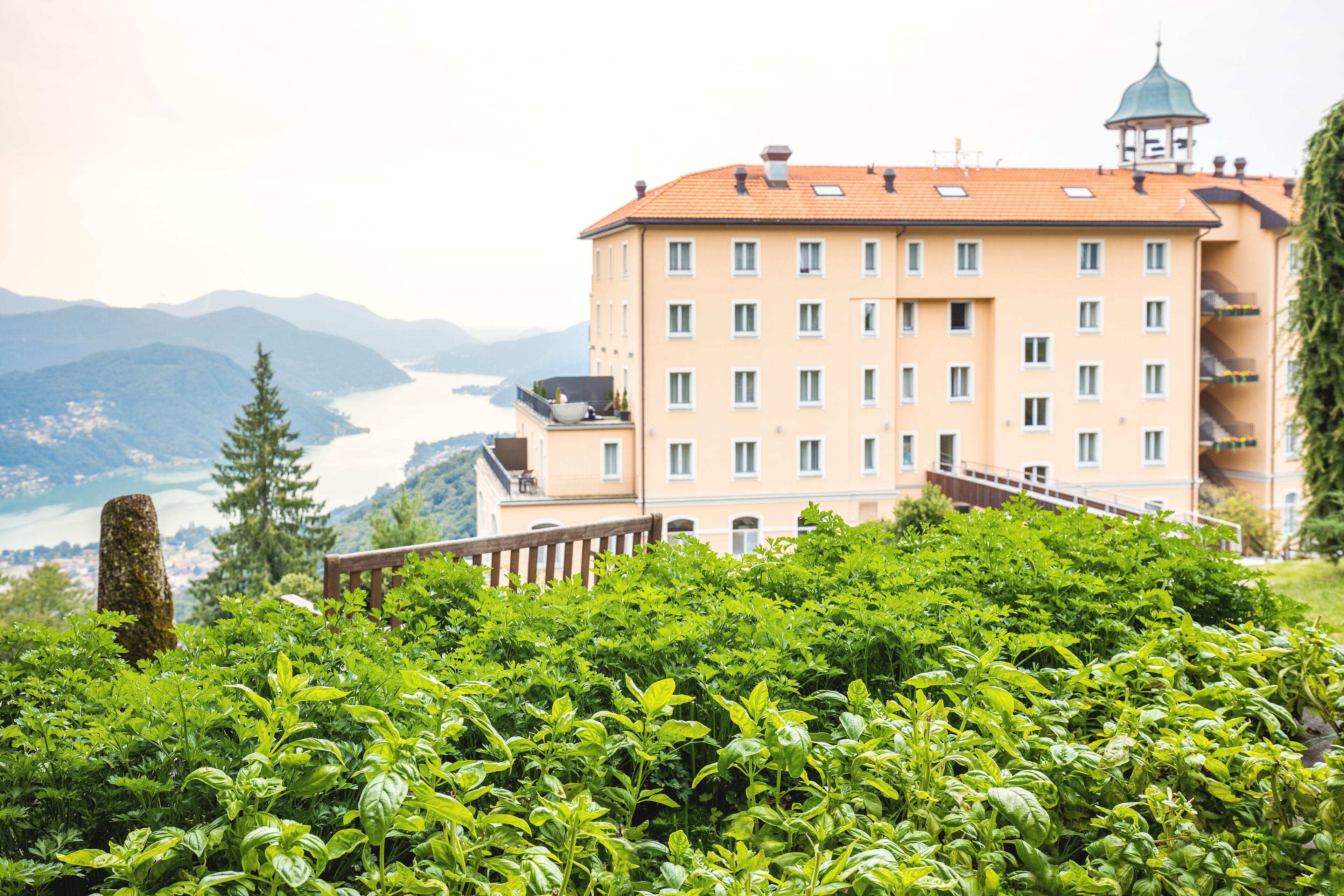 Ein mehrstöckiges Gebäude mit Balkon, umgeben von üppiger Vegetation und mit Blick auf ein Gewässer.