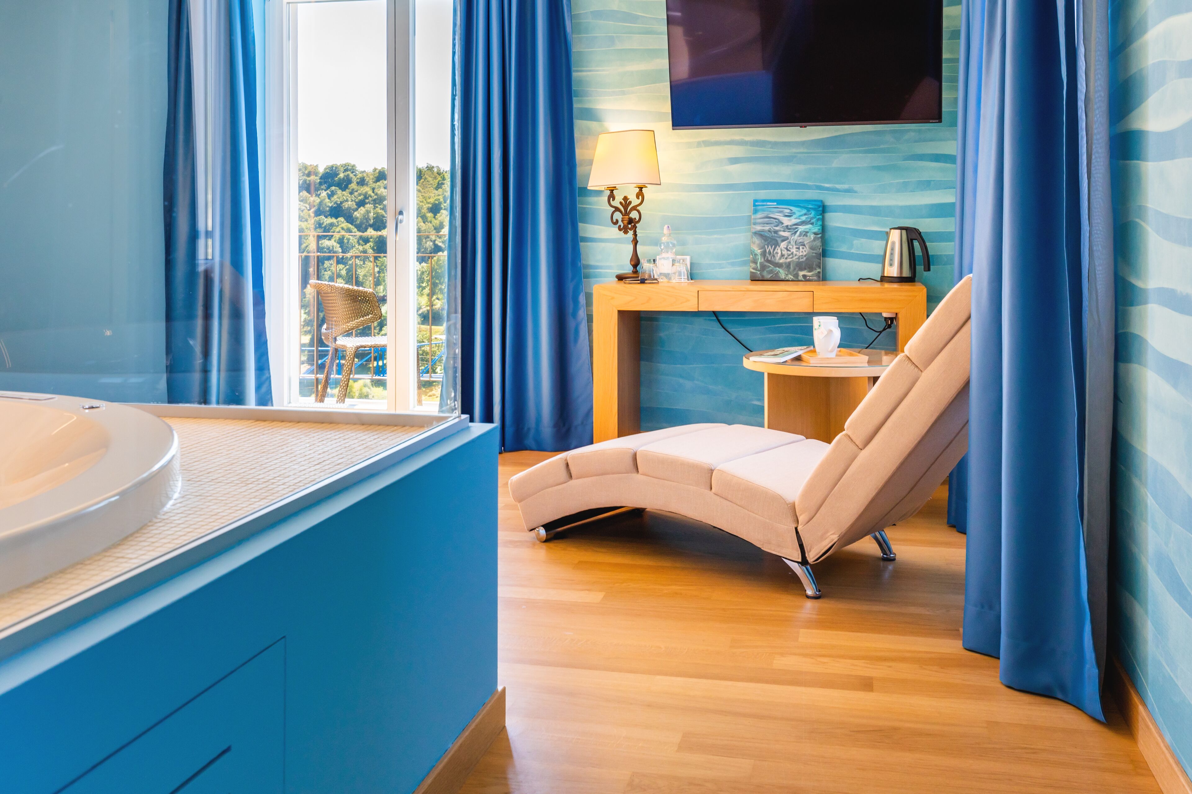 A modern bathroom with a bathtub, a vanity, a chair, and a television mounted on the wall.