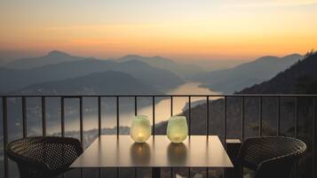 Balcón con una mesa y dos sillas, con vista a un paisaje montañoso que incluye un río.