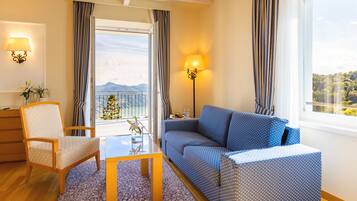 Habitación de hotel con sofá, sillón, mesa y balcón con cortinas.