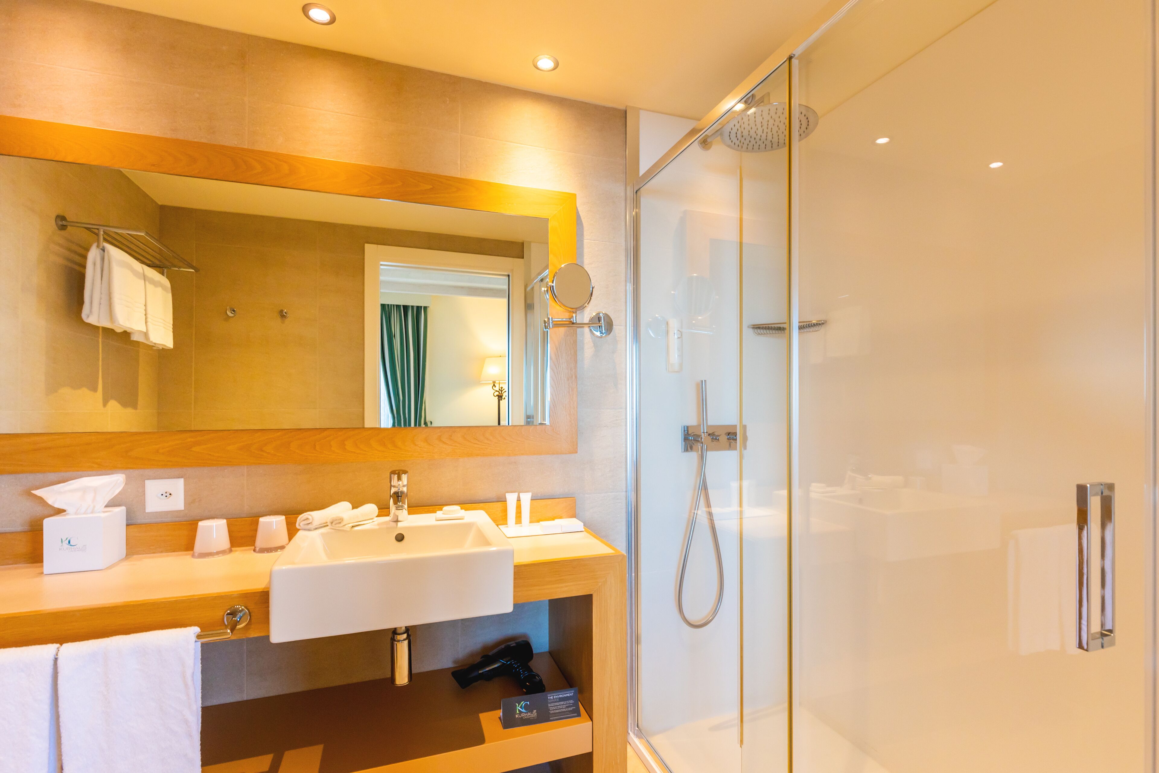 A modern bathroom with a glass-enclosed shower, a large mirror, and a wooden vanity with a sink and towel rack.