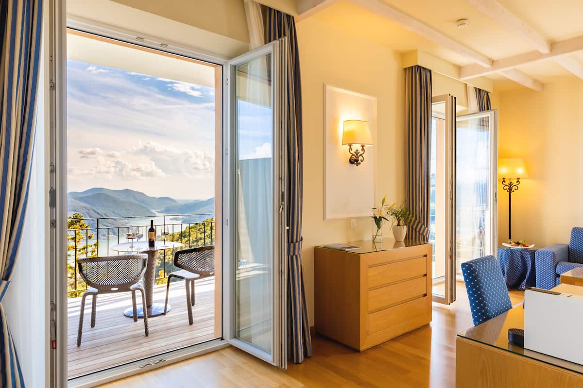 A modern hotel room with a balcony, a dining area, and a seating area with a view of the mountains.