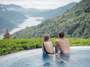 A couple sitting in a pool overlooking a lake and mountains.