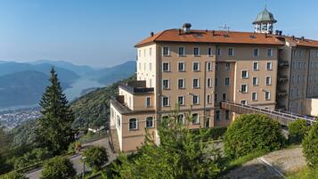A multi-story building with a red-tiled roof, a balcony, and a view of a lake and mountains.